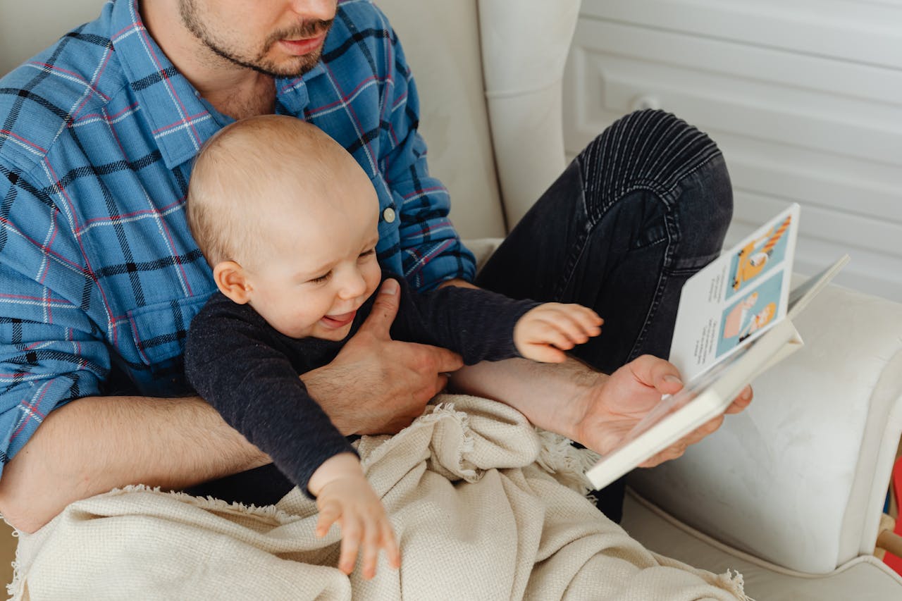 A father and his baby bonding while reading a book together indoors.